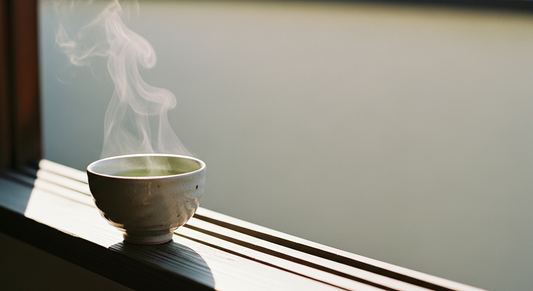 A single yunomi filled with pale green sencha beside a morning window
